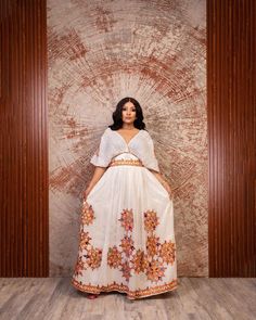 a woman standing in front of a wall wearing a white dress with orange flowers on it