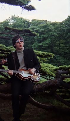 a man sitting on top of a tree holding a guitar