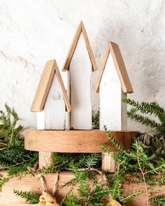 three wooden houses sitting on top of a table next to pine cones and greenery