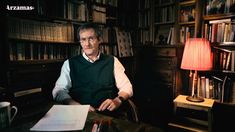 a man sitting at a desk in front of a book shelf with books on it