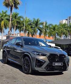 a grey bmw suv parked in a parking lot with palm trees and buildings behind it