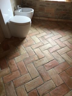 a bathroom with brick flooring and a toilet next to a window in the corner