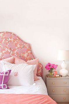 a bed with pink and white pillows on top of it's headboard next to two nightstands