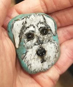 a hand holding a stone with a dog's face painted on it