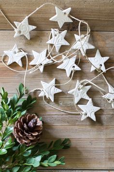 some white ornaments are hanging on a wooden table next to a pine cone and greenery