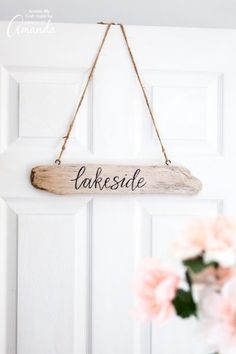 a wooden sign hanging from the side of a white door with flowers in front of it