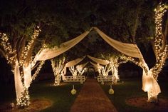 an outdoor wedding venue with white draping and lights on the trees at night