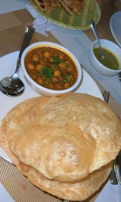 two pita breads on a plate next to a bowl of soup and silverware