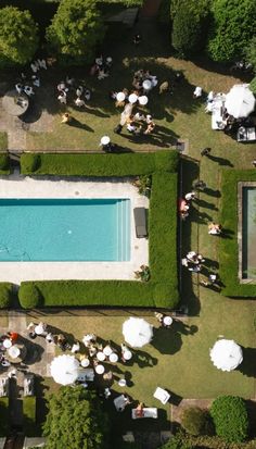 an aerial view of a pool surrounded by lawn chairs and umbrellas, with people sitting at tables next to it