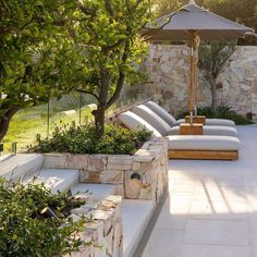 an outdoor patio with lounge chairs, trees and stone walls on either side of the pool