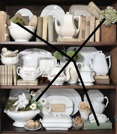 a book shelf filled with white dishes and other decorative items on top of eachother