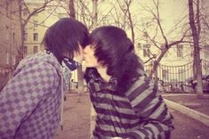 two young men kissing each other on the street in front of some trees and buildings