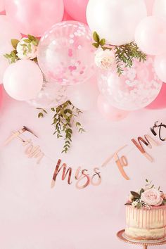 a cake with pink frosting and balloons in the background