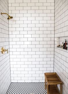 a white tiled shower with black and white floor tiles on the wall next to a wooden bench