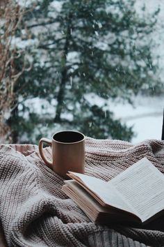 an open book sitting on top of a blanket next to a cup