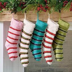 christmas stockings hanging from a mantel decorated with holly