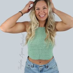 a woman with long blonde hair wearing a green crop top and blue denim shorts smiling