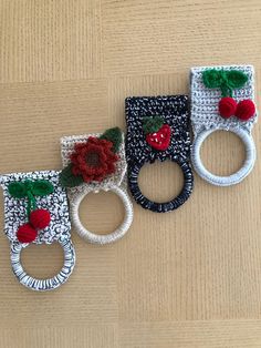 three crocheted rings with red flowers and green leaves are on a wooden surface