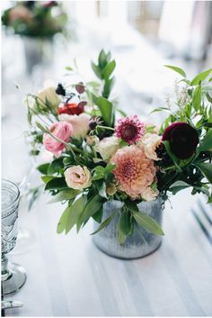 a vase filled with lots of flowers sitting on top of a table next to wine glasses