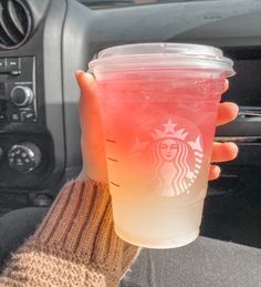 a person holding up a plastic cup in their hand while sitting in the drivers seat of a car