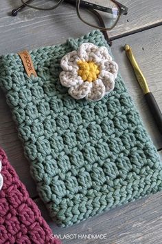 a crocheted pouch with a flower on it next to eyeglasses and a pen