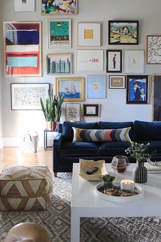 a living room filled with lots of pictures on the wall above a white coffee table