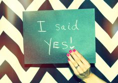 a woman holding up a sign that says i said yes on it in front of a chevron wall