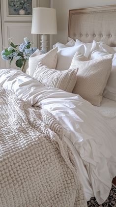 a bed with white linens and pillows in a bedroom next to a vase with flowers