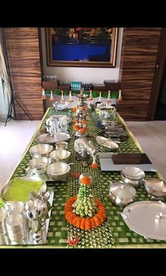 a long table is set up with silver dishes and orange flowers on the green checkered table cloth