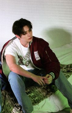 a young man sitting on top of a bed next to a green and white blanket