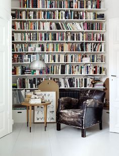 a living room filled with lots of books and furniture next to a wall mounted book shelf