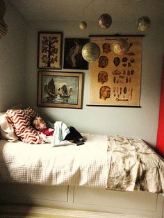 a small child is sleeping on a bed in a room with pictures and paintings above it