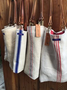 four bags hanging on a wooden wall with tags attached to the handles and bottoms