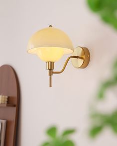 a wall light that is on the side of a wall next to a mirror and potted plant