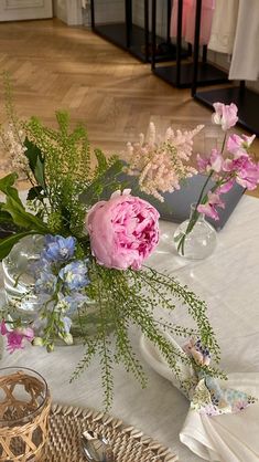 pink and blue flowers in glass vases on a white table cloth with silverware