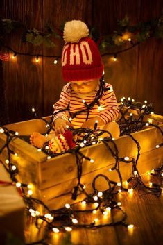 a small child wearing a red and white hat sitting in a box with christmas lights around it