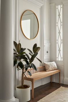 a wooden bench sitting in front of a mirror on the wall next to a potted plant