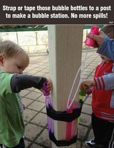 two small children are playing with some water bottles on a post while another child is holding onto the pole