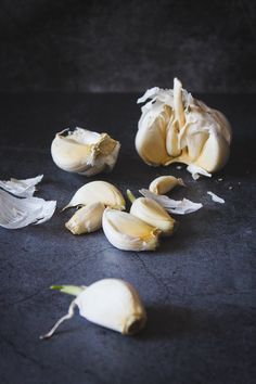 peeled garlic on a black surface with the peels still attached to it and whole heads