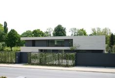 a modern house is shown on the side of the road in front of a fence