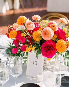 an arrangement of colorful flowers in a vase on a table with wine glasses and plates