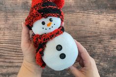 a hand holding a snowman ornament with a red hat and scarf on