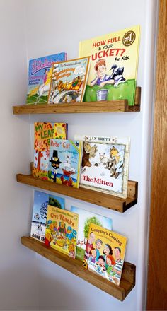 three wooden bookshelves with children's books on them in front of a white wall