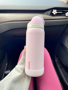 a person holding a pink water bottle in their hand while sitting in a car seat