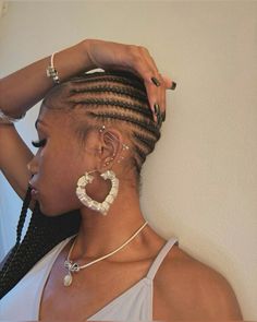 a woman with cornrows and earrings on her head, leaning against a wall