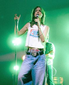 a woman singing into a microphone while standing in front of two other people on stage