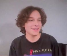 a young man with curly hair wearing a pink floyd t - shirt and looking at the camera