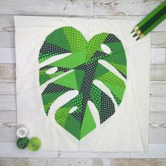 a green heart shaped paper piece next to two pencils on a white tablecloth