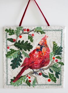 a red bird sitting on top of a green leaf covered wall hanging from a hook