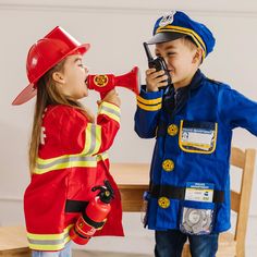 two children dressed in fireman costumes are playing with a toy phone and talking to each other